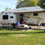 Family relaxing outside fifth-wheel RV with chairs and table at Sugar Sands RV Resort.